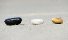 drei Steine in einer Reihe am feinen Sandstrand: schwarz, weiss und gelbbraun -  - Andreas Bertram-Weiss, Supervisor ǀ Mehr-Blick- Supervision - Teamsupervision